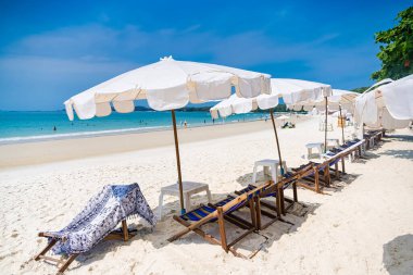 Rayong, Tayland - Nisan 01, 2025: Açık mavi gökyüzü altında sıralanmış renkli güverte sandalyeleri ve şemsiyeleri olan el değmemiş kumlu plaj, Koh Samet, Rayong, Tayland 'da okyanusun tadını çıkaran insanlar