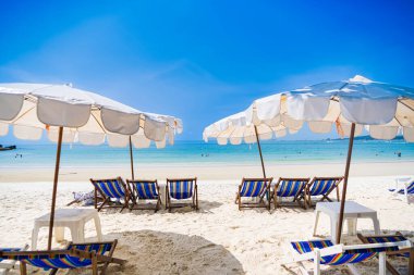 Rayong, Tayland - Nisan 01, 2025: Açık mavi gökyüzü altında sıralanmış renkli güverte sandalyeleri ve şemsiyeleri olan el değmemiş kumlu plaj, Koh Samet, Rayong, Tayland 'da okyanusun tadını çıkaran insanlar