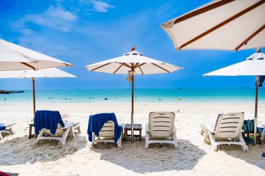 Rayong, Tayland - Nisan 01, 2025: Açık mavi gökyüzü altında sıralanmış renkli güverte sandalyeleri ve şemsiyeleri olan el değmemiş kumlu plaj, Koh Samet, Rayong, Tayland 'da okyanusun tadını çıkaran insanlar