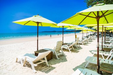 Rayong, Tayland - Nisan 01, 2025: Açık mavi gökyüzü altında sıralanmış renkli güverte sandalyeleri ve şemsiyeleri olan el değmemiş kumlu plaj, Koh Samet, Rayong, Tayland 'da okyanusun tadını çıkaran insanlar