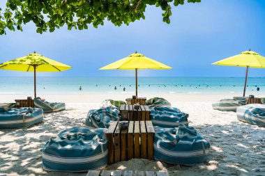 Rayong, Tayland - Nisan 01, 2025: Açık mavi gökyüzü altında sıralanmış renkli güverte sandalyeleri ve şemsiyeleri olan el değmemiş kumlu plaj, Koh Samet, Rayong, Tayland 'da okyanusun tadını çıkaran insanlar
