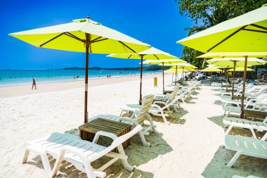 Rayong, Tayland - Nisan 01, 2025: Açık mavi gökyüzü altında sıralanmış renkli güverte sandalyeleri ve şemsiyeleri olan el değmemiş kumlu plaj, Koh Samet, Rayong, Tayland 'da okyanusun tadını çıkaran insanlar