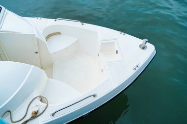 Oturma alanı olan beyaz bir motorlu tekne pruvasının üst görüntüsü görünür halatlar ve metal teçhizatlarla yeşil suya kenetlenmiş.