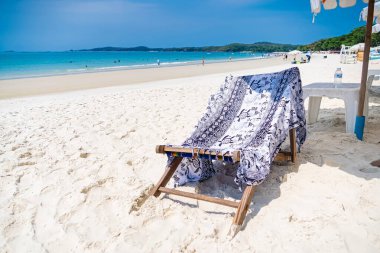 Rayong, Tayland - Nisan 01, 2025: açık mavi gökyüzünün altında turkuaz denizi gören, beyaz kumsalda desenli bir sandalyenin olduğu plaj sahnesi.