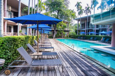 Rayong, Tayland - Nisan 01, 2025: Güneşli bir günde modern tatil köyleri ve yüksek palmiye ağaçları ile çevrili lüks açık yüzme havuzu
