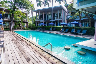 Rayong, Tayland - Nisan 01, 2025: Güneşli bir günde modern tatil köyleri ve yüksek palmiye ağaçları ile çevrili lüks açık yüzme havuzu