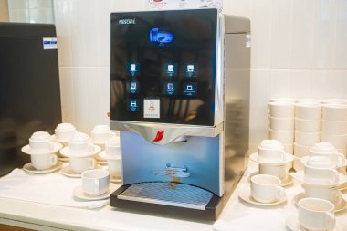 Rayong, Tayland - Nisan 01, 2025: Bir otel lobisinde beyaz seramik fincanlar düzgünce dizilmiş modern dokunmatik kahve makinesi