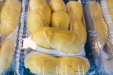 Temiz bir plastik kabın içine yerleştirilmiş durian meyvesinin yakın çekimi, parlak sarı et ve beyaz yenilebilir tohumlar sergiliyor.