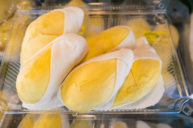 Temiz bir plastik kabın içine yerleştirilmiş durian meyvesinin yakın çekimi, parlak sarı et ve beyaz yenilebilir tohumlar sergiliyor.