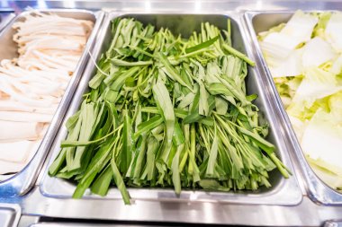 Taze yeşil yapraklı sebzeler bir salata barında ya da açık büfede metal bir tepside sergilenir.