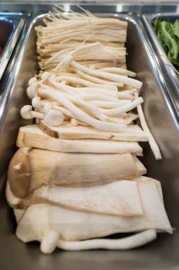 Açık büfedeki veya salata barındaki paslanmaz çelik bir tepsiye yerleştirilmiş enoki ve kral istiridyesi de dahil olmak üzere çeşitli taze mantarlar.