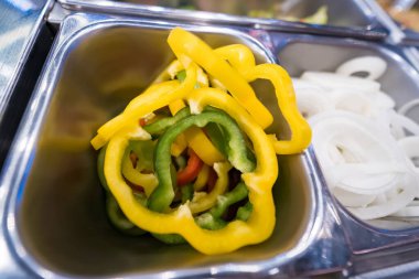 Dilimlenmiş sarı, yeşil ve kırmızı dolmalık biberleri bir salata barında paslanmaz çelik yemek tepsisinde yakın plan.