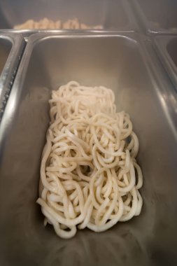 Açık büfede ya da restoranda servis edilen paslanmaz çelik yemek tepsisinde taze pişmiş beyaz udon eriştesi.