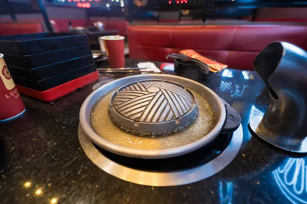 Kore barbekü tepsisi bir restoranda bir masada. Etrafında metal ızgara ve et suyu var. Yanında sosla pişirilmeye hazır.