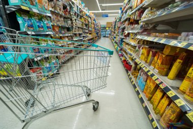 Bangkok, Tayland - 30 Mayıs 2025: Bangkok, Tayland 'da çeşitli paketlenmiş ürünler ve ev eşyalarıyla dolu bir market koridorunda bir alışveriş arabası.