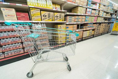 Bangkok, Tayland - 30 Mayıs 2025: Bangkok, Tayland 'da çeşitli paketlenmiş ürünler ve ev eşyalarıyla dolu bir market koridorunda bir alışveriş arabası.