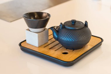 Geleneksel dökme demir çaydanlık ve siyah bardak beyaz bir yüzeye yerleştirilmiş modern bambu tepsisi üzerinde.