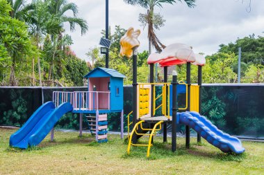 Ağaçlarla çevrili tropikal bir açık hava parkında slaytlarla ve tırmanan çerçevelerle renkli çocuk parkı seti.
