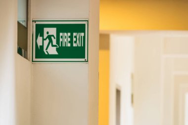 Koridordaki duvarda yeşil bir yangın çıkışı tabelası. Yumuşak ışıklandırma sıcak bir atmosfer yaratıyor.