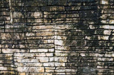 Doğal ve dokulu yıpranmış bir yüzeye sahip düzensiz şekilli taşlar içeren eski bir taş duvarın yakın çekimi.