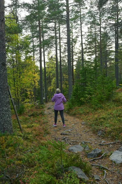 A woman in a jacket walks in the autumn forest and talks on the phone.
