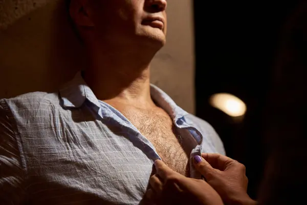 Female hands seductively unbutton a shirt on a hairy male chest