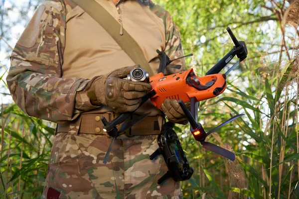 A military drone operator holds a broken quadcopter and a drone camera in his hands.
