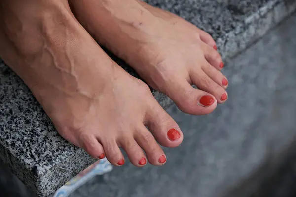 Female feet with nails painted with red varnish. Woman standing on a marble step in the city