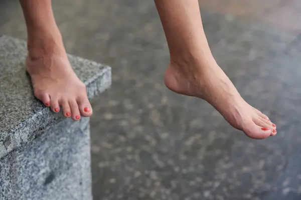 Female feet with nails painted with red varnish. Woman taking a step from a marble step in the city