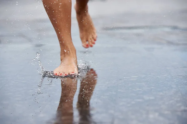 Women\'s feet make splashes in puddles on the road in the city.