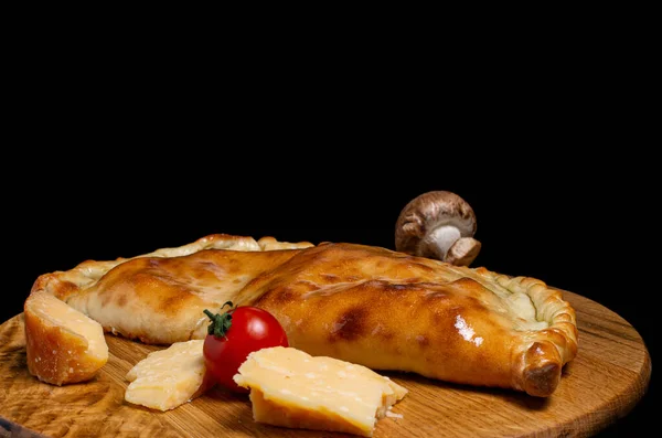 カルゾーネはピザを木のキッチンボードにシャンピニョンキノコチェリートマトパルメザンチーズ 黒い背景に隔離された ストック画像