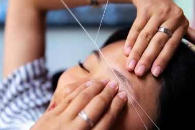 detail of an eyebrow waxing with threading on a young woman in a beauty salon, concept of wellness and body care clipart