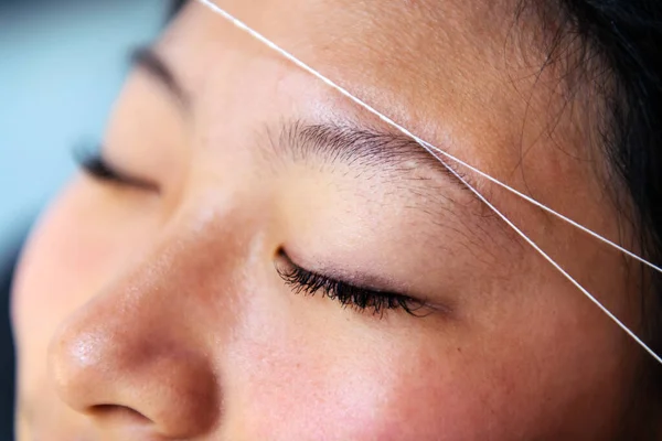 detail of an eyebrow waxing with threading on a young woman in a beauty salon, concept of wellness and body care
