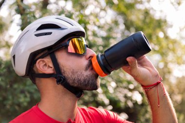 Genç adam kask takıyor ve bisiklet gözlükleri takıyor şişesinden su içiyor, özgürlük ve spor anlayışı doğada