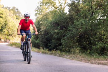 Genç bisikletçi, dağ bisikletiyle bir orman yolunda, doğada özgürlük ve spor kavramında rahatça seyahat ediyor.