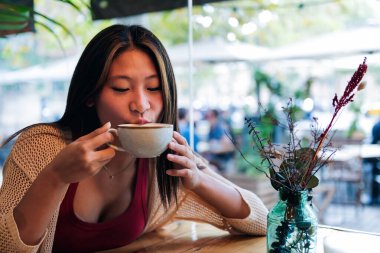 young asian woman drinking coffee in a coffee shop, concept of relaxation and leisure