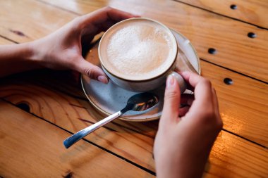 close-up of a womans hands holding a cup of coffee on a wooden table, concept of relaxation and leisure