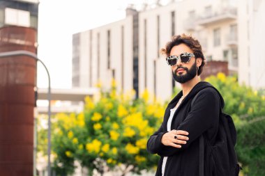 portrait of a beautiful young man with beard and fashionable sunglasses looking at camera with arms crossed, concept of urban lifestyle and stylish clothing, copy space for text