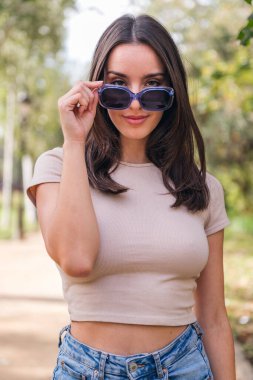 young caucasian woman looking at camera with mischief over her sunglasses, concept of youth and beauty