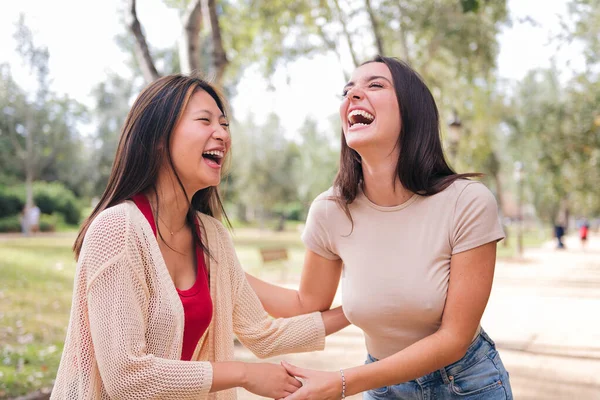 couple of young women laughing during a date in a park, concept of friendship and love between people of the same sex