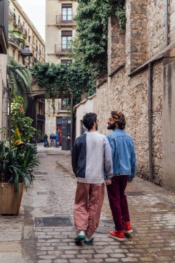 rear view of a gay male couple strolling happy down a ancient street holding hands, concept of leisure and love between people of the same sex