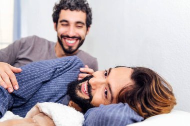 Gey erkek çift yatakta dinleniyor ve sabah mutlu gülümsüyor. Gerçek insan yaşam tarzı ve aynı cinsiyetten insanlar arasındaki aşk kavramı.