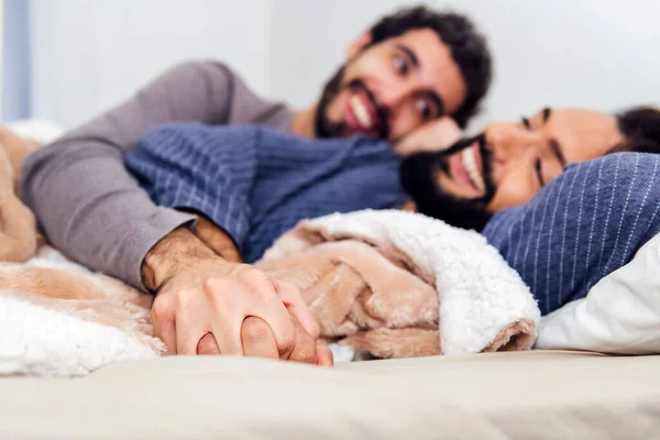 stock image detail of the hands of a couple of gay men intertwined on the bed, concept of real people lifestyle and love between people of the same sex