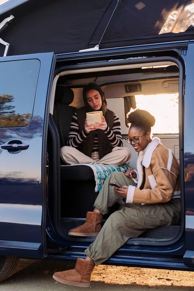 Duas Jovens Mulheres Apreciando Vida Campista Van Leitura Pôr Sol — Fotografia de Stock