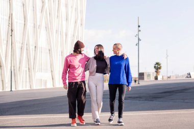 Üç arkadaş, bir erkek ve iki kadın, güneşli bir günde yürürken kucaklaşıyorlar, arkadaşlık ve şehir yaşam tarzı kavramı.