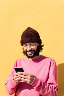 Gülümseyen genç adam sarı arka planda cep telefonu kullanıyor, iletişim ve modern yaşam tarzı kavramı, metin için kopyalama alanı