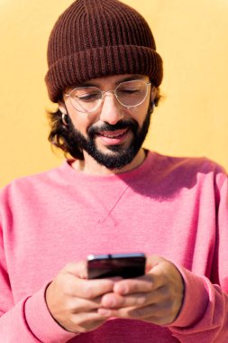 Sarı arka planda cep telefonu kullanan gülümseyen bir gencin portresi, iletişim teknolojisi ve modern yaşam tarzı kavramı