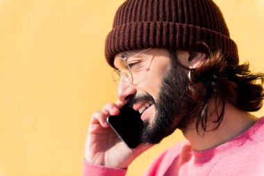 Sarı arka planda cep telefonuyla konuşan gülümseyen genç adam, iletişim ve modern yaşam tarzı kavramı, metin için kopyalama alanı