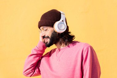 Genç adam kulaklıklarındaki müziğin keyfini çıkarıyor. Arka planda sarı bir duvar, ritim kavramı ve olumlu insanlar, metin için kopyalama alanı.