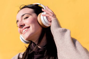 Sarı arka planda kulaklıkla müzik dinleyen gülümseyen genç kadın, ritim kavramı ve pozitif insanlar.